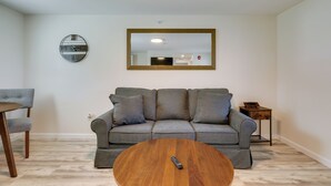 A living room with a grey sofa, a round wooden coffee table, a round mirror, and a small side table. - 3 Mi to Beach & Pier: Pet-Friendly Cape Cod Apt! (Wareham)