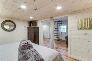 A bedroom with a bed, a dresser, a mirror, and a spiral staircase leading to another room.