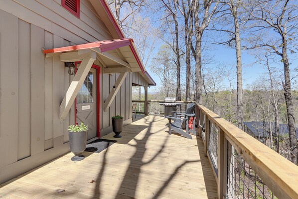 Une terrasse en bois avec une porte rouge, un barbecue et un pot de fleurs.
