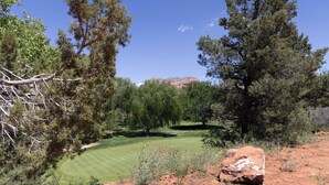 Campo de golfe com um caminho bem definido, rodeado por árvores e uma grande rocha em primeiro plano.
