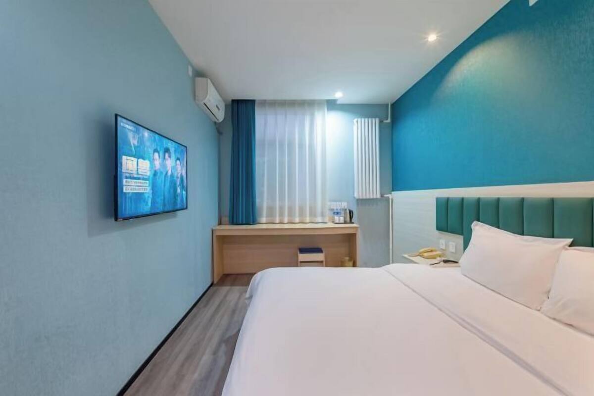Quarto de hotel com cama, escrivaninha, televisão e janela com cortinas.