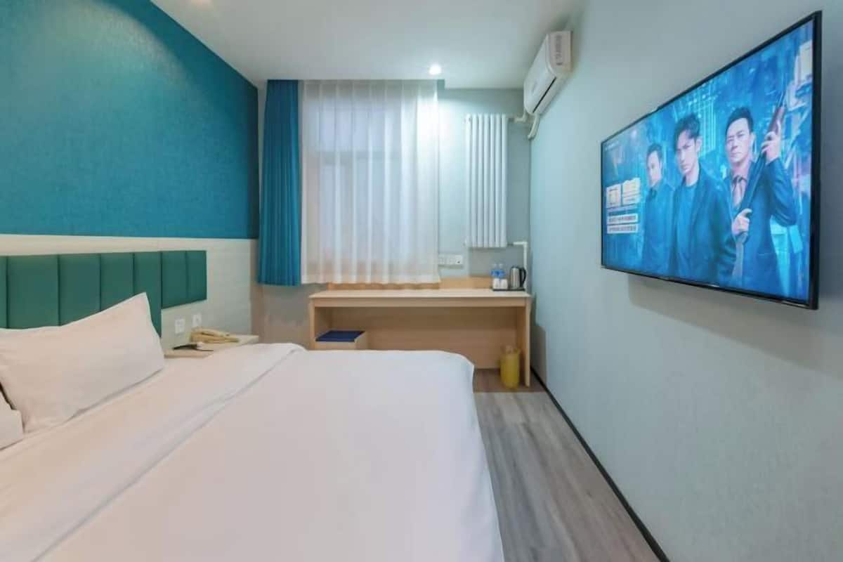 Quarto de hotel com cama, escrivaninha, televisão e janela com cortinas.