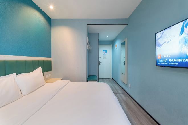 A hotel room with a bed, a TV mounted on the wall, and a door leading to another room.