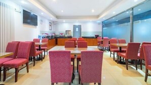 A dining area with red upholstered chairs and tables, a kitchen in the background, and a flat-screen TV mounted on the wall. - Lilai Hotel (Wendu Shuicheng store, Beijing) (Beijing)
