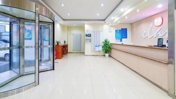 A hotel reception area with a glass partition, a reception desk, a potted plant, and a wall-mounted clock. - Lilai Hotel (Wendu Shuicheng store, Beijing) (Beijing)