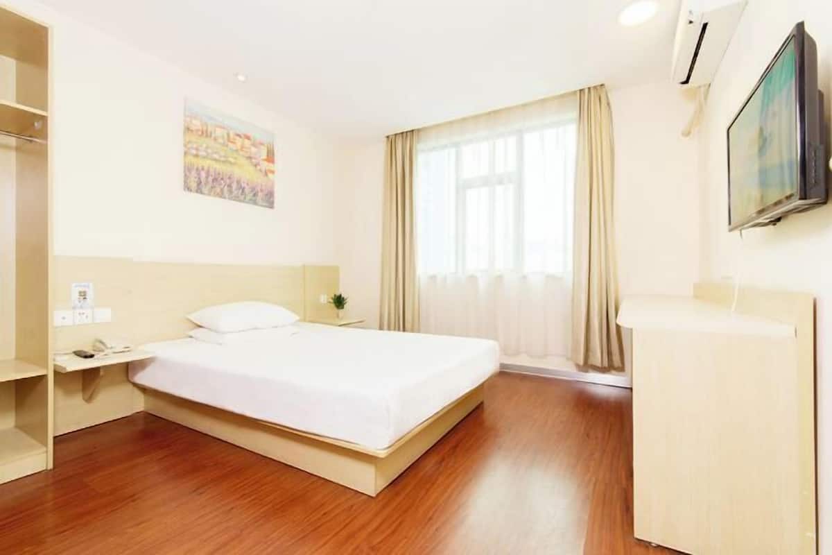 Quarto de hotel com cama, mesa de cabeceira, televisão e janela com cortinas.