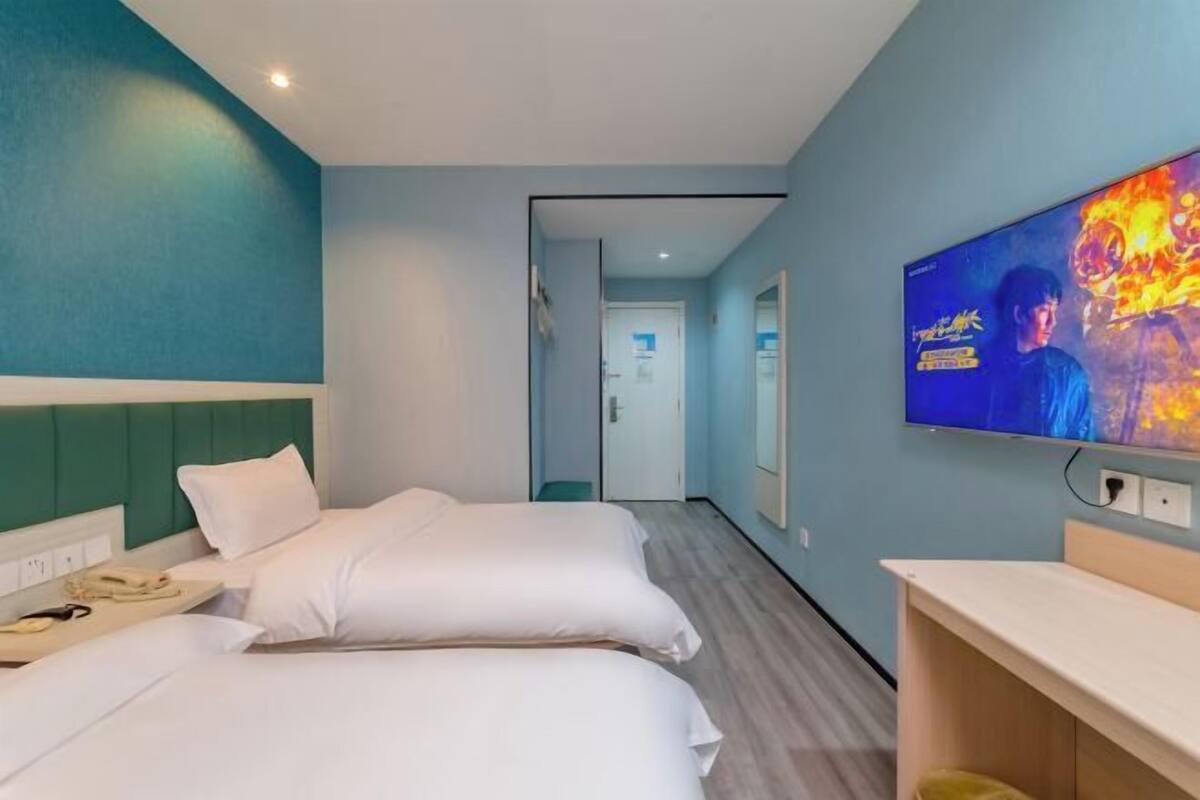 Quarto de hotel com duas camas, uma televisão na parede e uma escrivaninha.