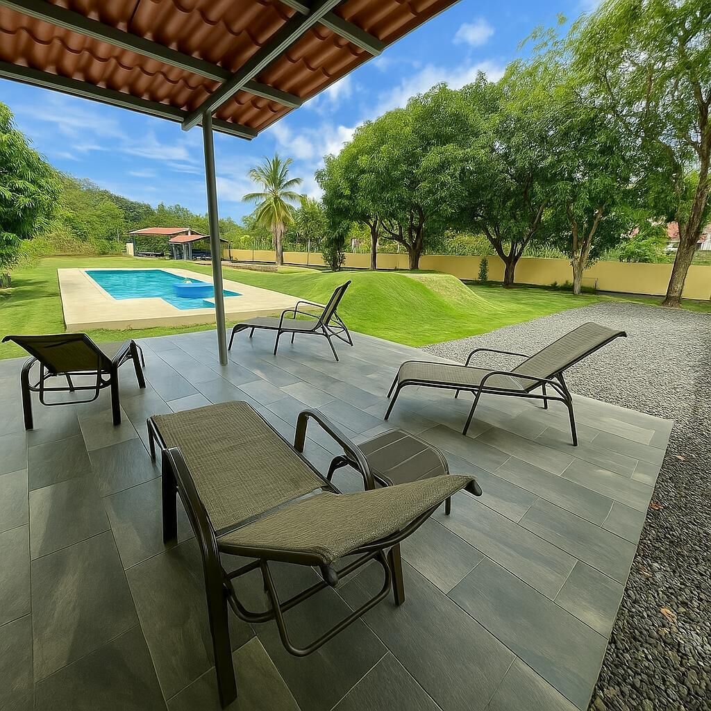 Une terrasse couverte avec des chaises longues et une piscine en arrière-plan.
