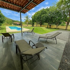 Een overdekt terras met lounge fauteuils en een zwembad op de achtergrond.