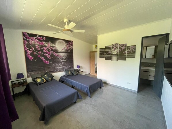 Une chambre avec deux lits, un ventilateur de plafond, une table de chevet, une lampe et un grand tableau floral accroché au mur.