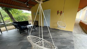 A covered patio with a hanging chair, a sofa, and a dining table. - Casa Fofo Family House (San Carlos)