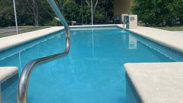 Una piscina con barandilla de metal, rodeada de una solana de hormigón y árboles.