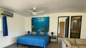 A bedroom with a bed, a ceiling fan, an air conditioning unit, a nightstand, a sofa, and a large window with curtains. - Casa Fofo Family House (San Carlos)