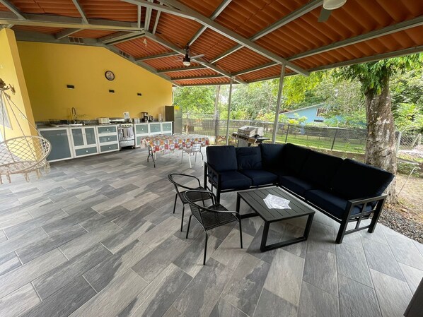 Un patio cubierto con mesa de comedor, sillas, sofá y zona de barbacoa.