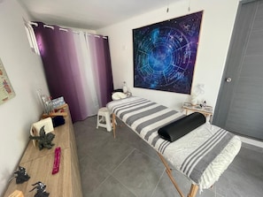 Een slaapkamer met een bed, een bureau, een stoel, een klein krukje, een paars gordijn en een wandtapijt.