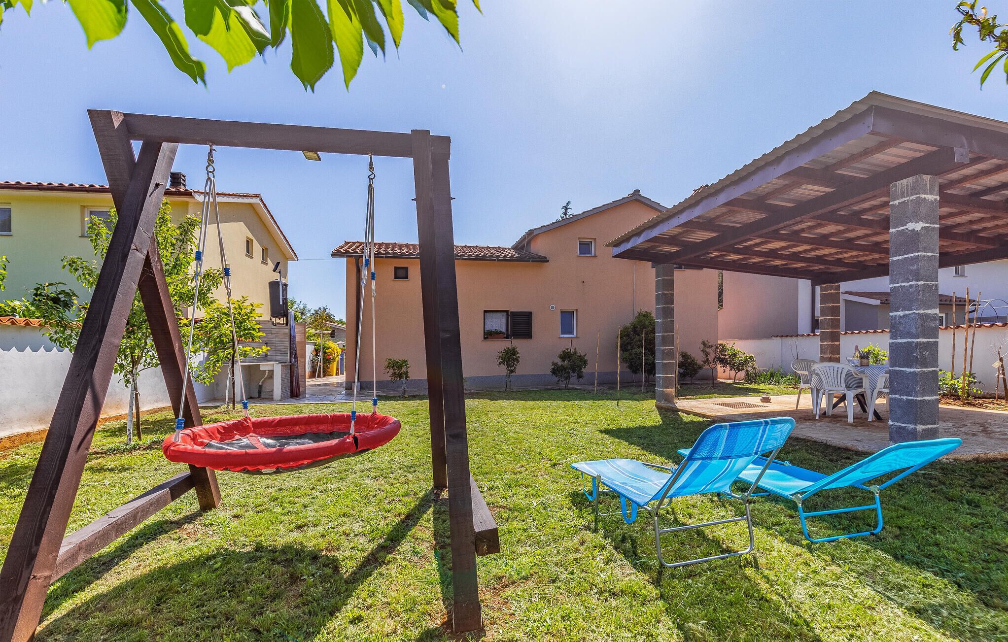 A backyard with a swing set, a red tire swing, and two blue lawn chairs.