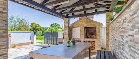 A covered patio with a table and chairs, a brick oven, and a small wooden structure.