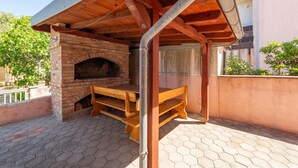 An outdoor brick oven with a wooden bench and table, surrounded by a tiled patio. - Beautiful apartment in Povljana with WiFi (Povljana)
