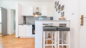 A modern kitchen with white cabinets, a granite countertop, and a stainless steel range hood. There are two bar stools with black cushions. - Beautiful apartment in Povljana with WiFi (Povljana)
