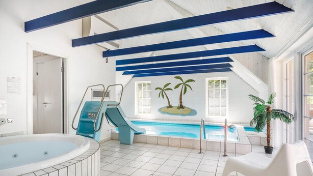 Une piscine intérieure avec un toboggan, un jacuzzi et une fresque représentant des palmiers.