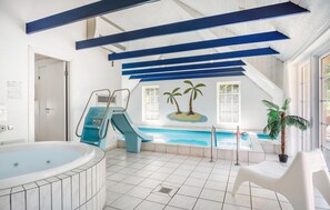Una piscina interna con uno scivolo, una vasca idromassaggio e un murale con palme.
