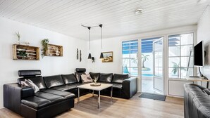 Un salon moderne avec un canapé d’angle en cuir noir, une table basse et une grande fenêtre donnant sur des palmiers.