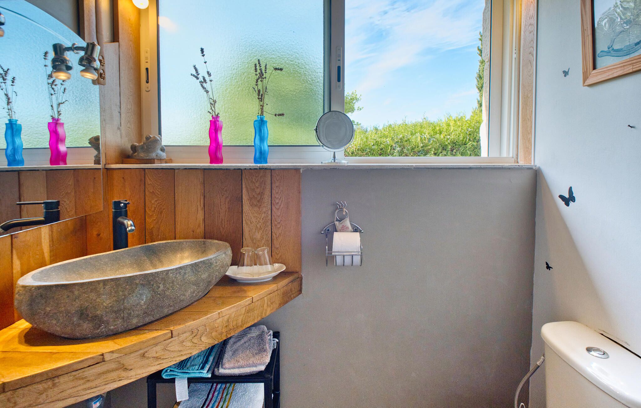 Un baño con un lavabo de piedra, encimera de madera y ventana con vistas a la vegetación.