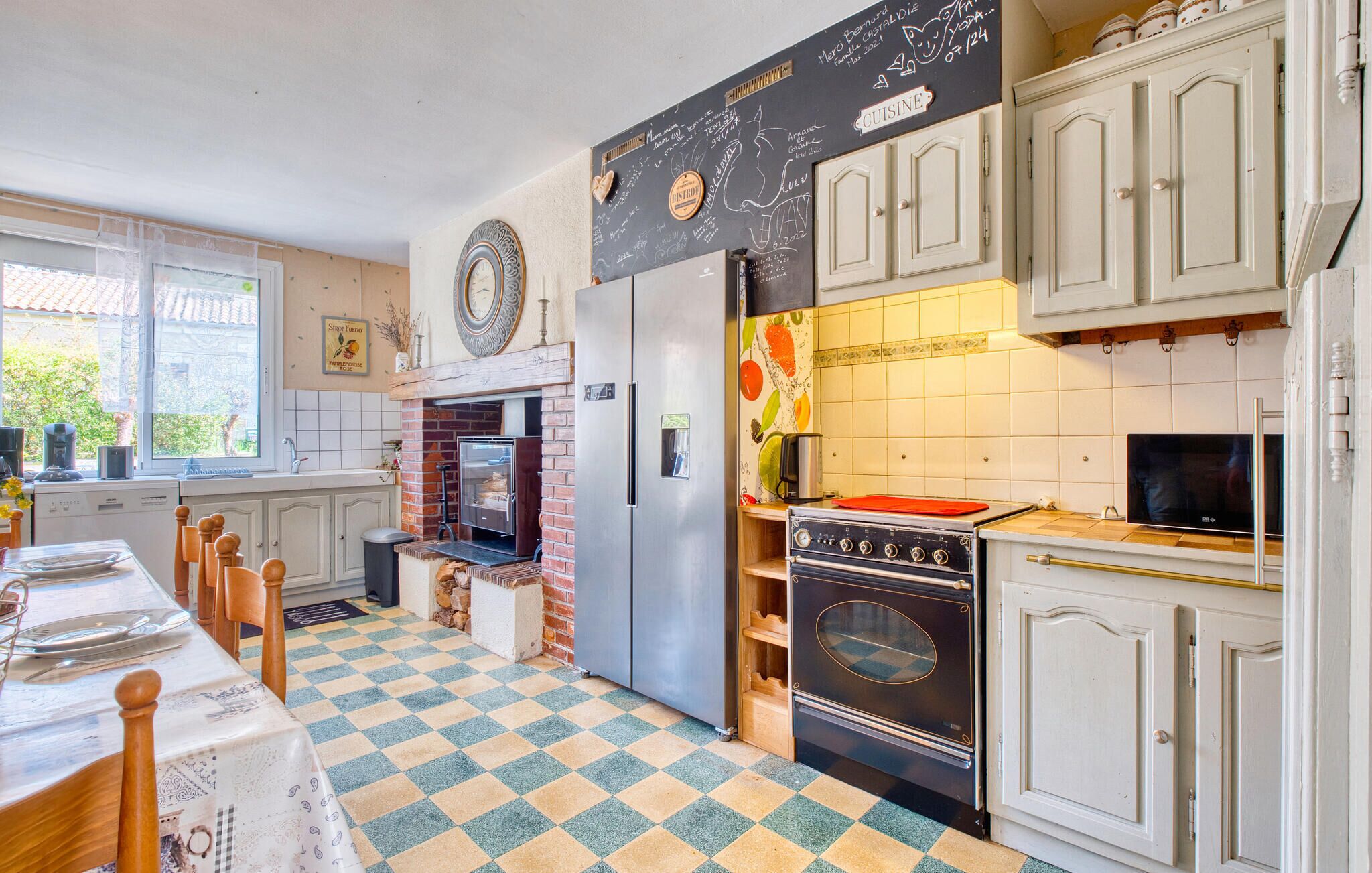 A kitchen with a checkered floor, a brick oven, a refrigerator, and white cabinets.