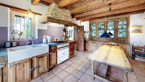 A rustic kitchen with wooden beams, a large wooden table, and a window with a view of the outdoors.