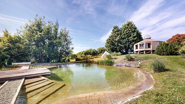 A lakeside property with a wooden dock, a tent, and a house with a dome roof.