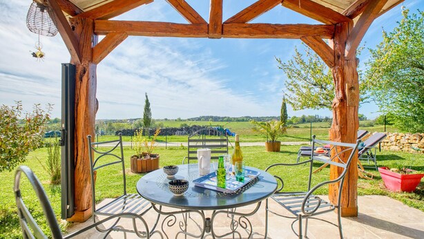 A covered outdoor seating area with a table and chairs, overlooking a rural landscape. - 2 bedroom awesome home in Les Lèches (Les Lèches)