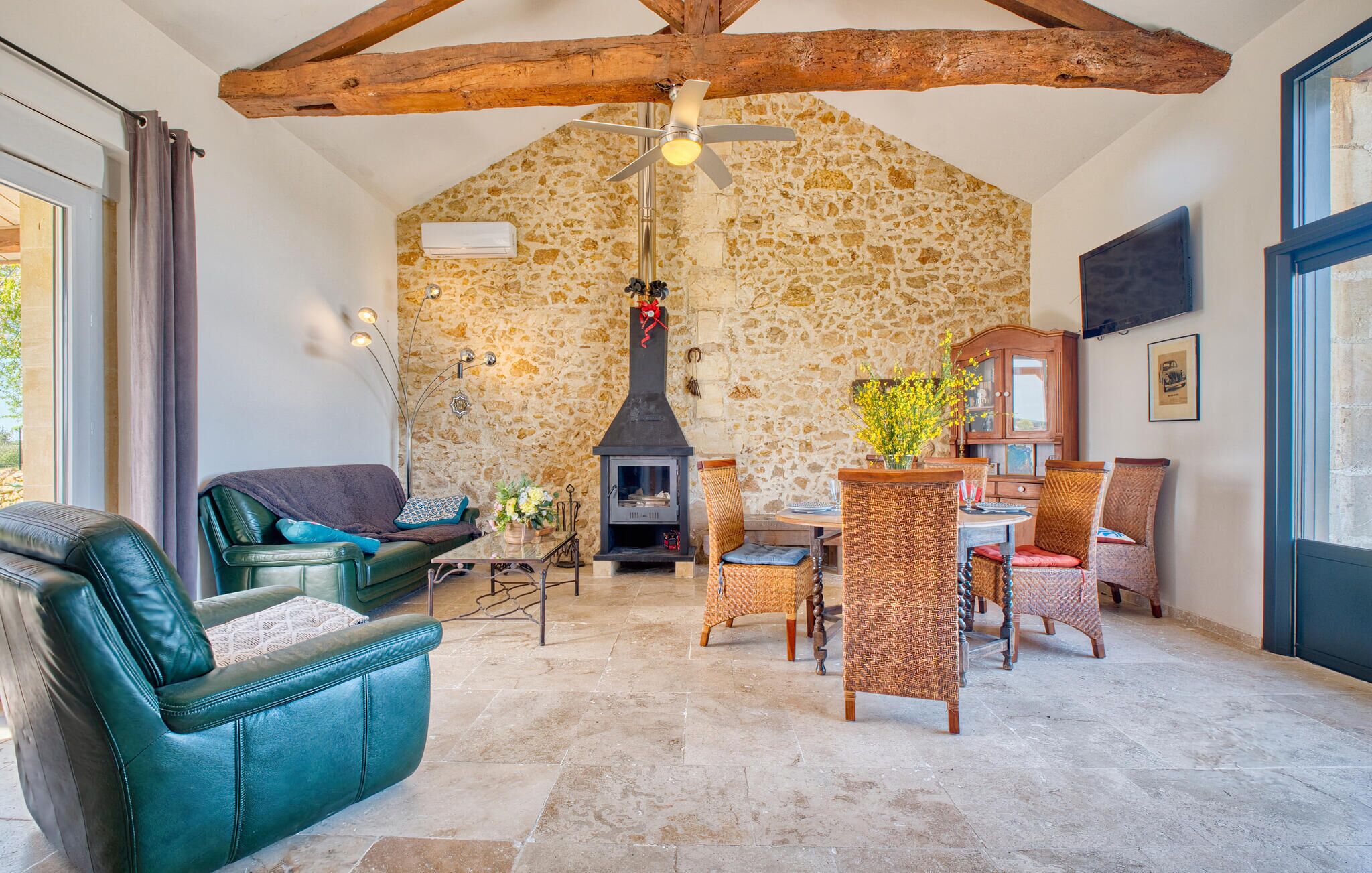 Un salon chaleureux avec un mur en pierre, une cheminée, des meubles en cuir et des fauteuils en osier.