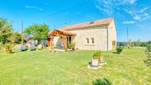 A stone house with a tiled roof, a wooden pergola, and a grassy yard with potted plants and outdoor furniture. - 2 bedroom awesome home in Les Lèches (Les Lèches)