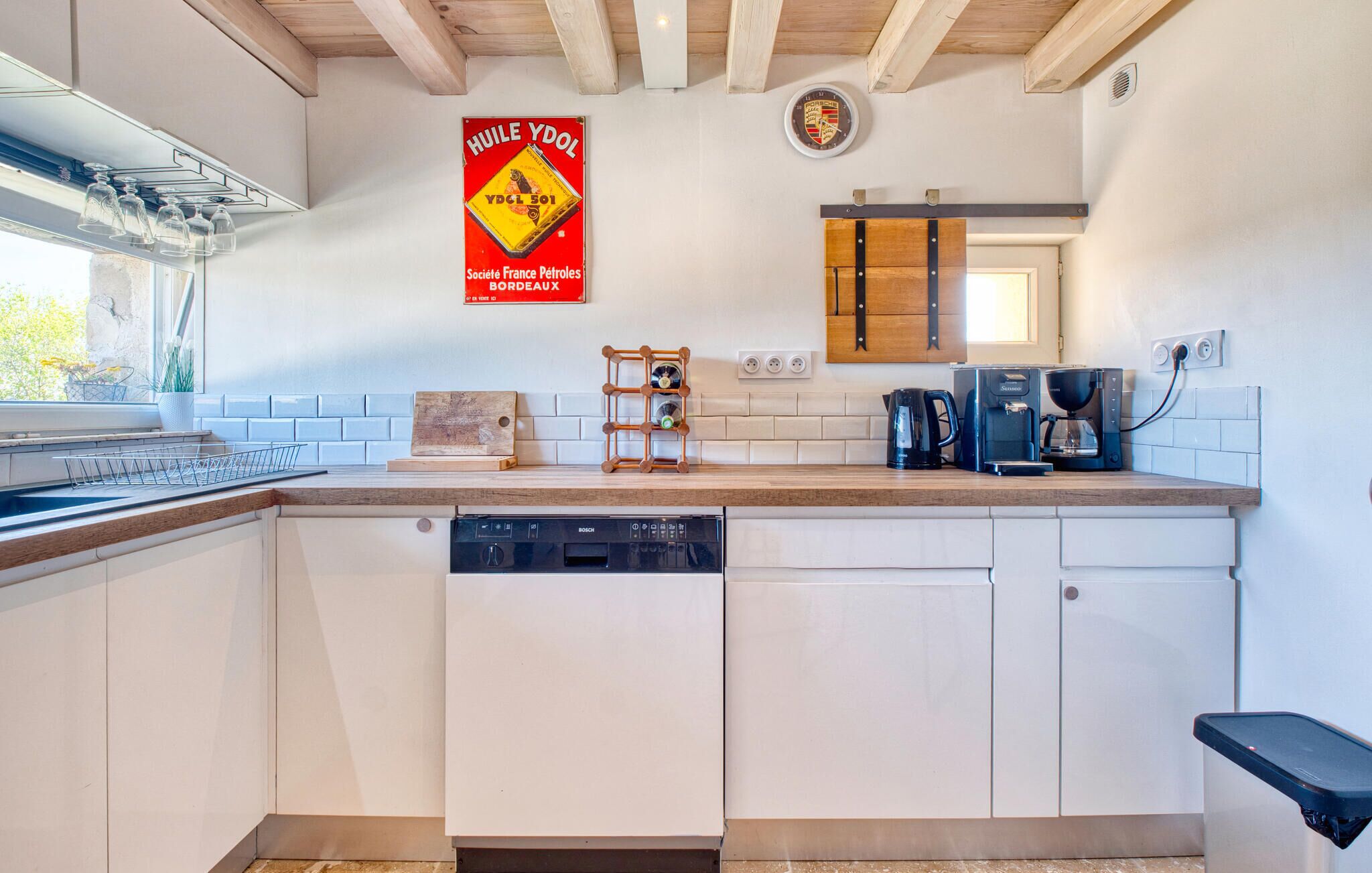 A modern kitchen with white cabinets, a Bosch dishwasher, a coffee maker, and a clock on the wall.