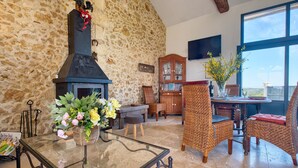 A rustic interior with a stone wall, a fireplace, wicker furniture, and a dining area with a view. - 2 bedroom awesome home in Les Lèches (Les Lèches)