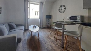 Un espace de vie compact comprenant un canapé, une petite table ronde, une kitchenette équipée d’un four à micro-ondes et une horloge murale.