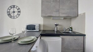 Une cuisine de taille réduite équipée d’un four à micro-ondes, d’un évier et d’une horloge murale.