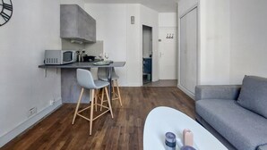 Un espace de vie compact comprenant un coin cuisine, un coin repas avec deux chaises, un canapé et une table basse agrémentée d’objets décoratifs.