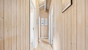 Un couloir étroit aux murs et au plancher en bois, qui mène à une pièce dont la porte se trouve au fond.