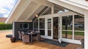 Une terrasse couverte avec une table et des chaises, de grandes portes-fenêtres coulissantes et une vue sur le jardin arrière.