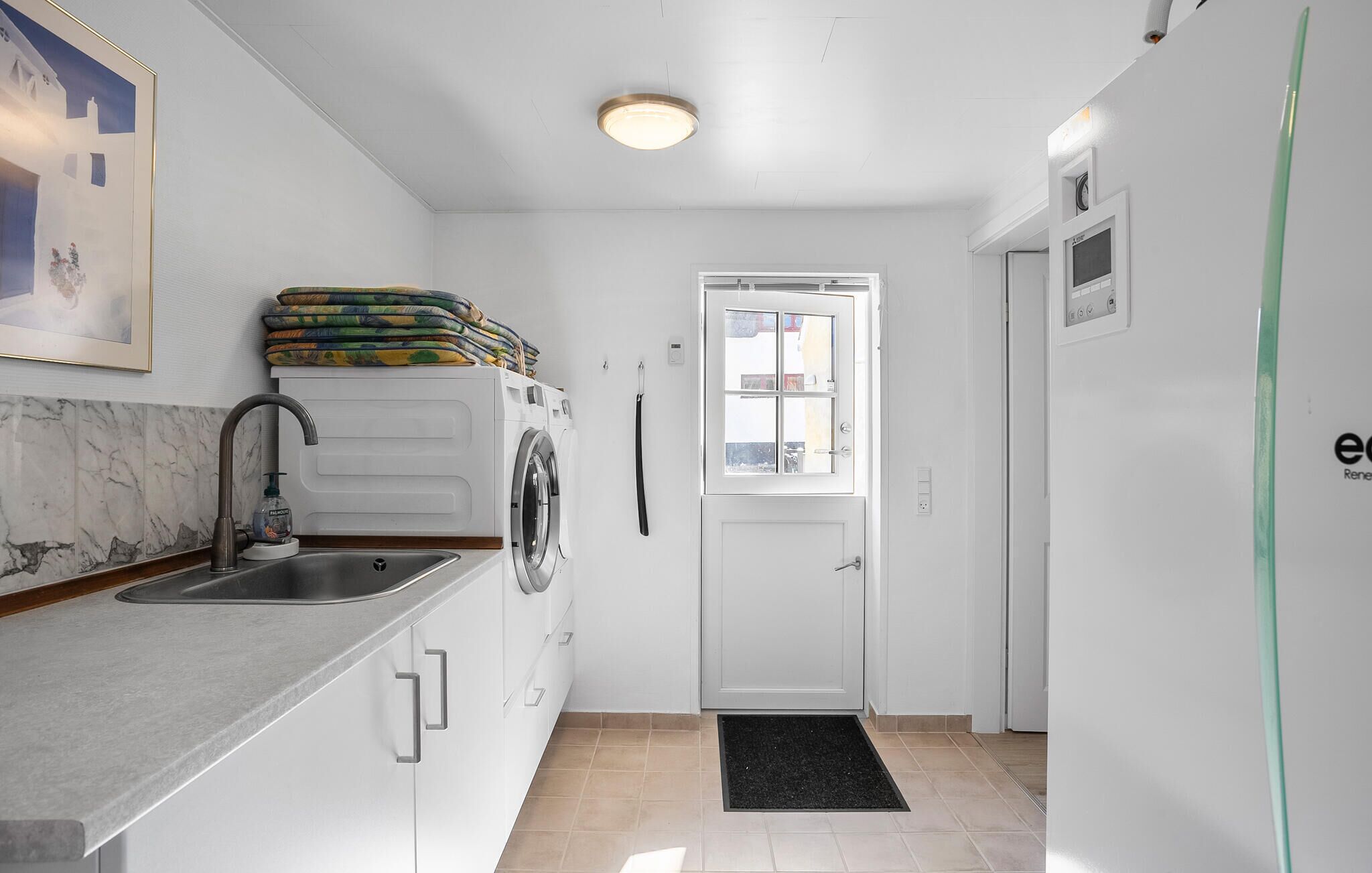 Een kleine keuken met een spoelbak, een wasmachine en een deur naar een andere kamer.
