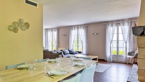 Un comedor con una mesa de madera dispuesta para cuatro, un sofá al fondo y vistas a zonas verdes.