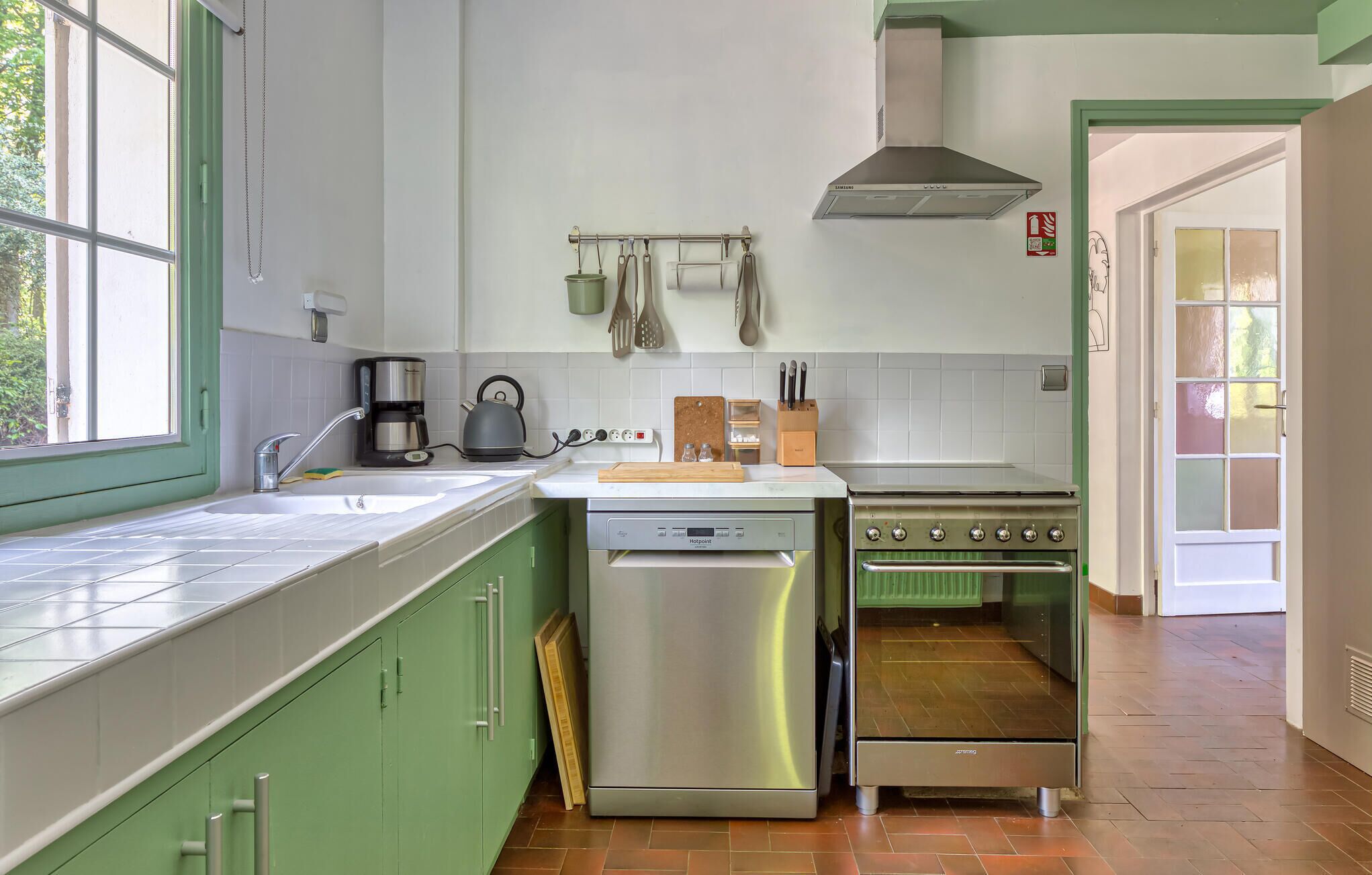 Une cuisine avec des meubles de rangement verts, un lave-vaisselle en acier inoxydable, une cuisinière et une machine à café.