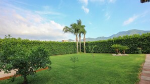 A well-maintained grassy area with palm trees and a hedge, with mountains in the background. - Villa Angela Holiday Apartment (Angri)