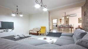 A living room with a grey sofa, a yellow armchair, a flat-screen TV, and a dining area with a table and chairs. - Villa Angela Holiday Apartment (Angri)
