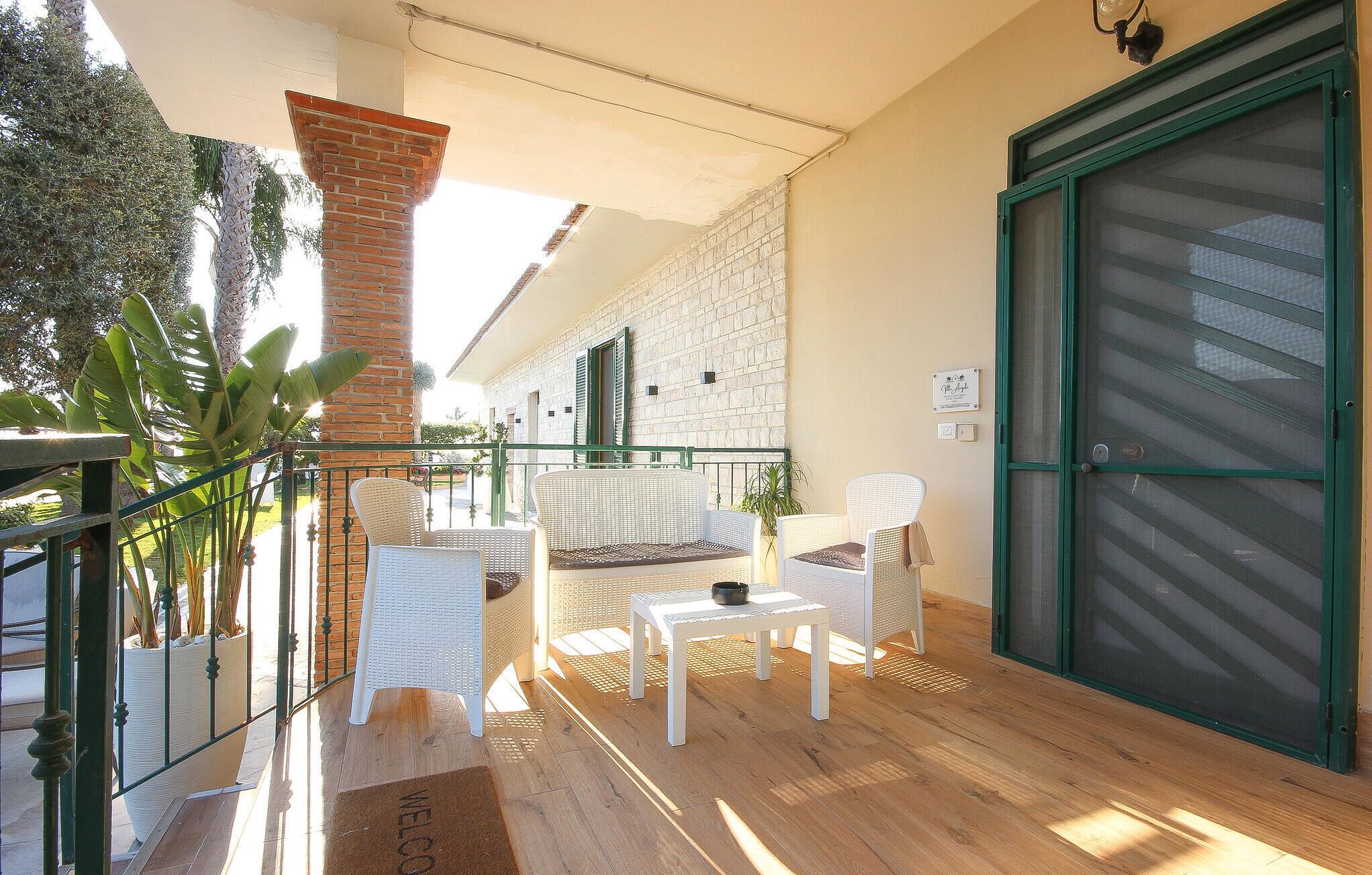 A balcony with wicker furniture, a brick pillar, and a green door.