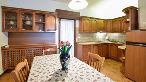 Une cuisine avec des meubles de rangement en bois, une table à manger recouverte d’une nappe à motifs floraux et un vase rempli de fleurs.