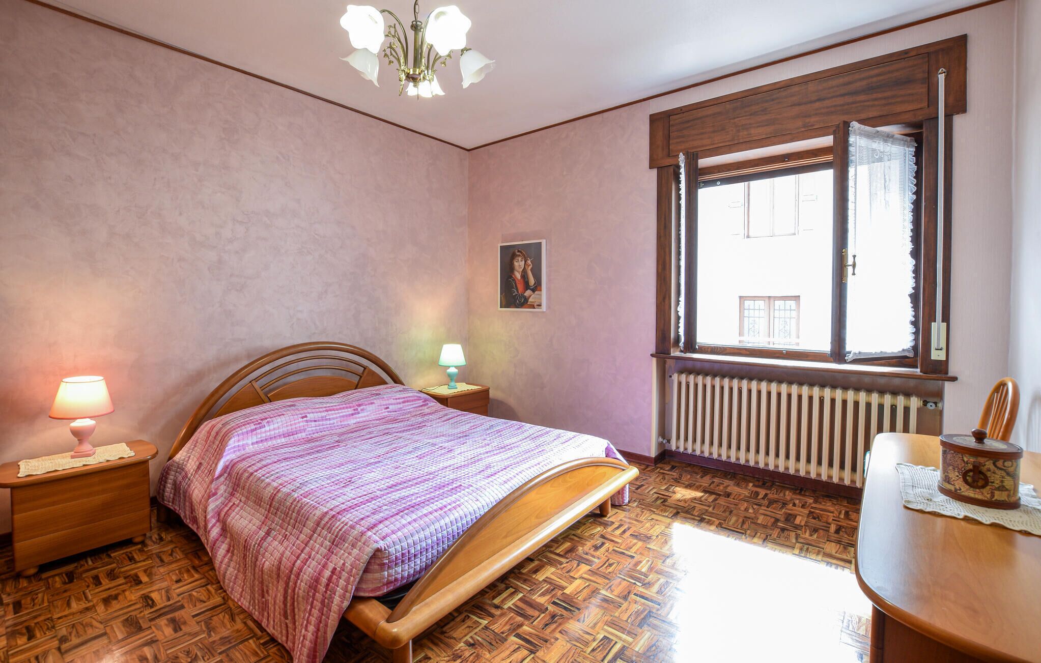 Une chambre à coucher avec un lit en bois, deux lampes de chevet, un radiateur, une fenêtre avec des rideaux et un plancher en bois.