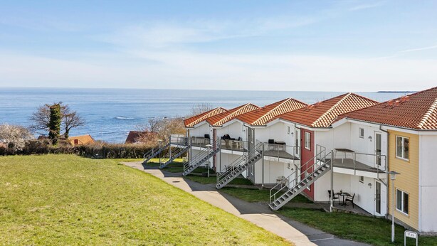 Un hotel costaner amb diverses habitacions, teulades vermelles, terrasses exteriors i vista al mar.