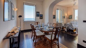 Een eetruimte met een tafel voor vier personen, houten stoelen en uitzicht op zee door grote ramen.